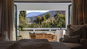 Un dormitorio con una cama, una silla, una mesita y vistas a un paisaje montañoso a través de una ventana.