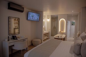Habitación de hotel con cama, escritorio con teléfono, televisor, baño con ducha y espejo.