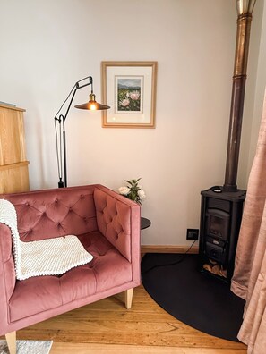Een gezellige woonkamer met een roze bank, een ingelijste foto aan de muur, een staande lamp en een houtkachel.