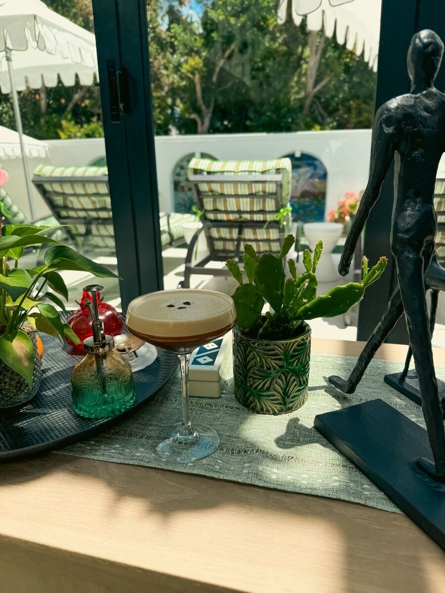 A table with a cactus plant, a bottle, a glass with a drink, and a small figurine.