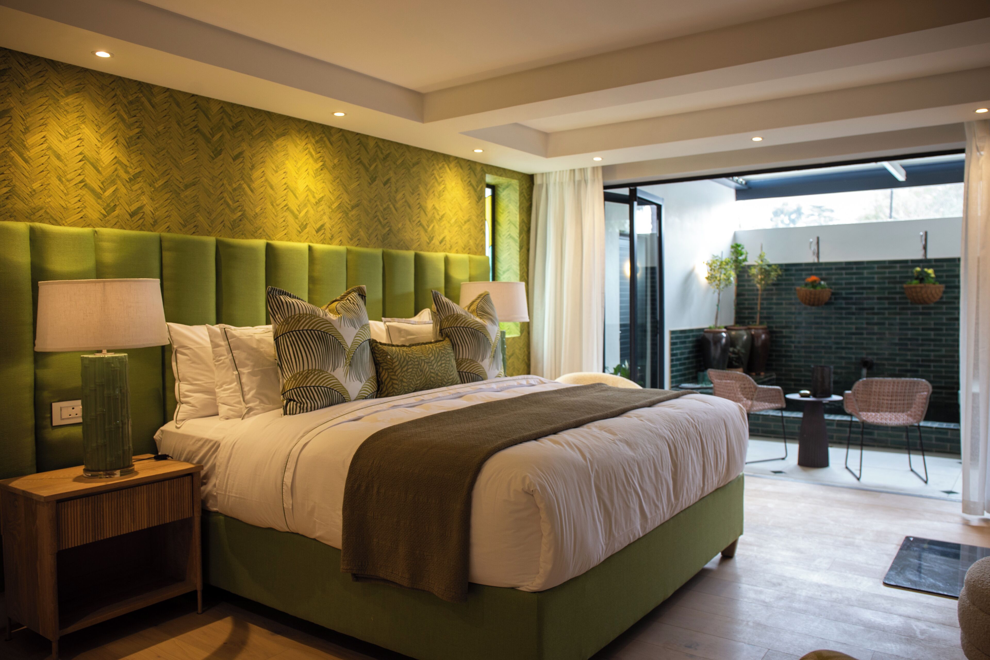 Un dormitorio moderno con una cama grande, cabecera verde y vistas a un patio exterior.