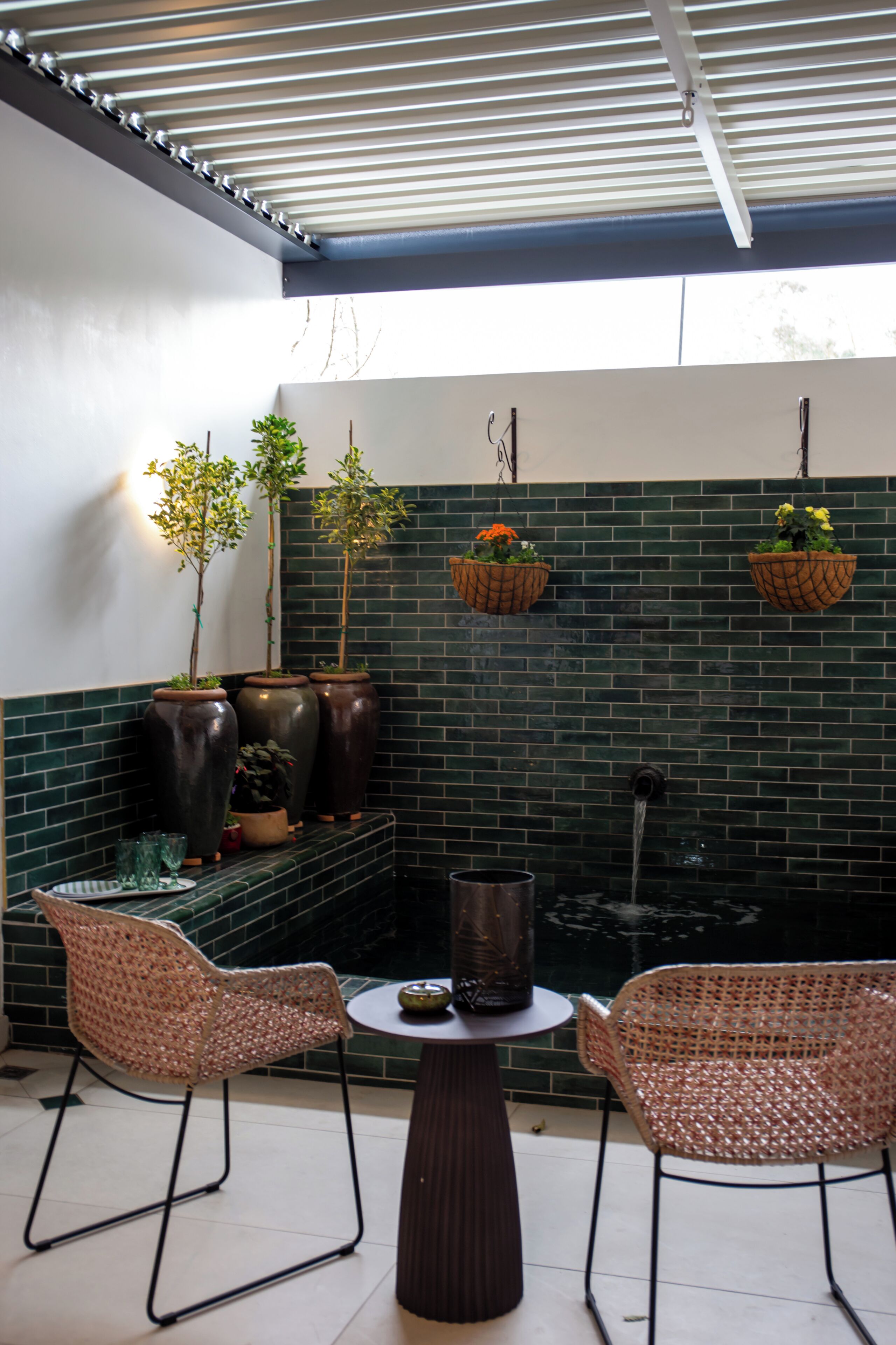Een terras met wickerstoelen, een ronde tafel en hangmanden met bloemen.