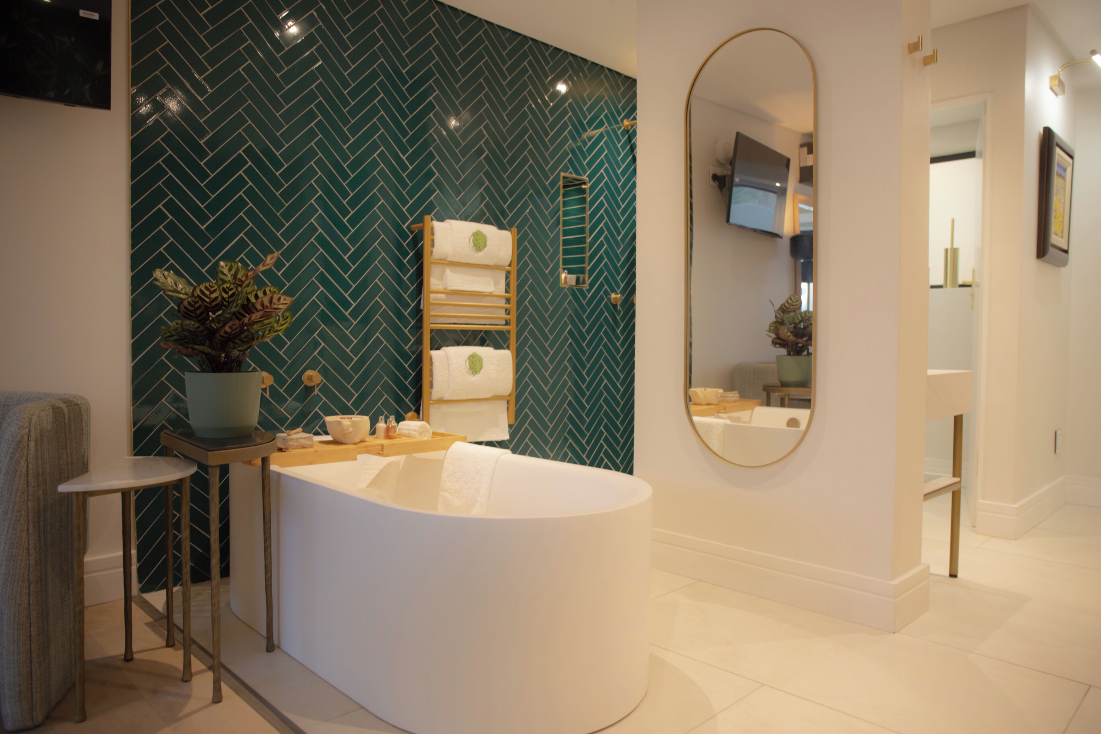 Um banheiro moderno com painel de azulejos em padrão herringbone, uma banheira livre, uma pequena mesa com produtos de higiene pessoal e um espelho.