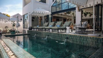 Un área de piscina moderna al aire libre con sillones de descanso y un edificio con cerramientos de vidrio.