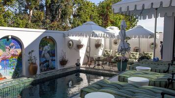 Zona de piscina con asientos, sombrillas y decoración mural.