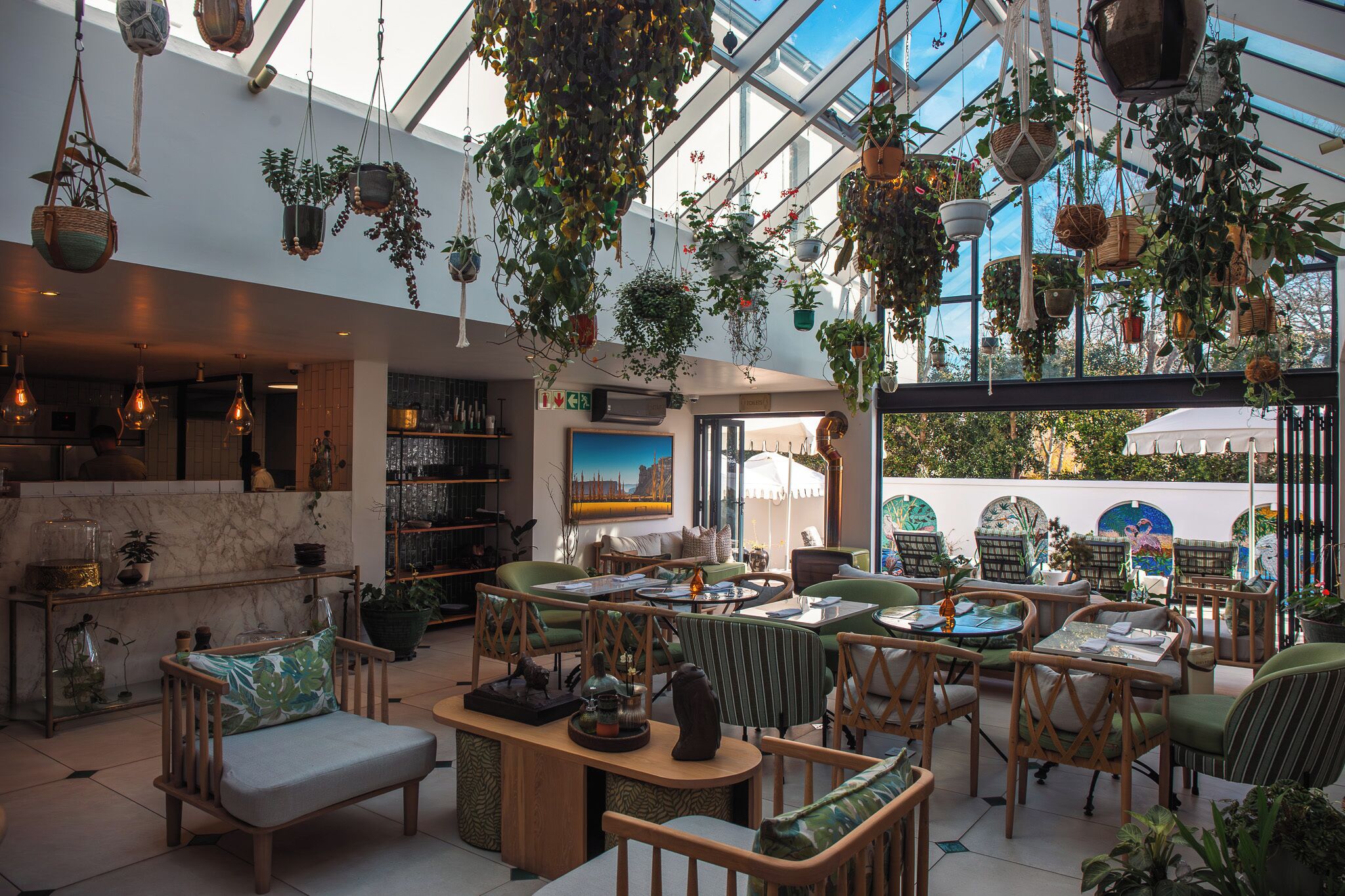 Amplio espacio interior con plantas colgantes, arreglos de asientos y vistas a través de un techo de cristal.