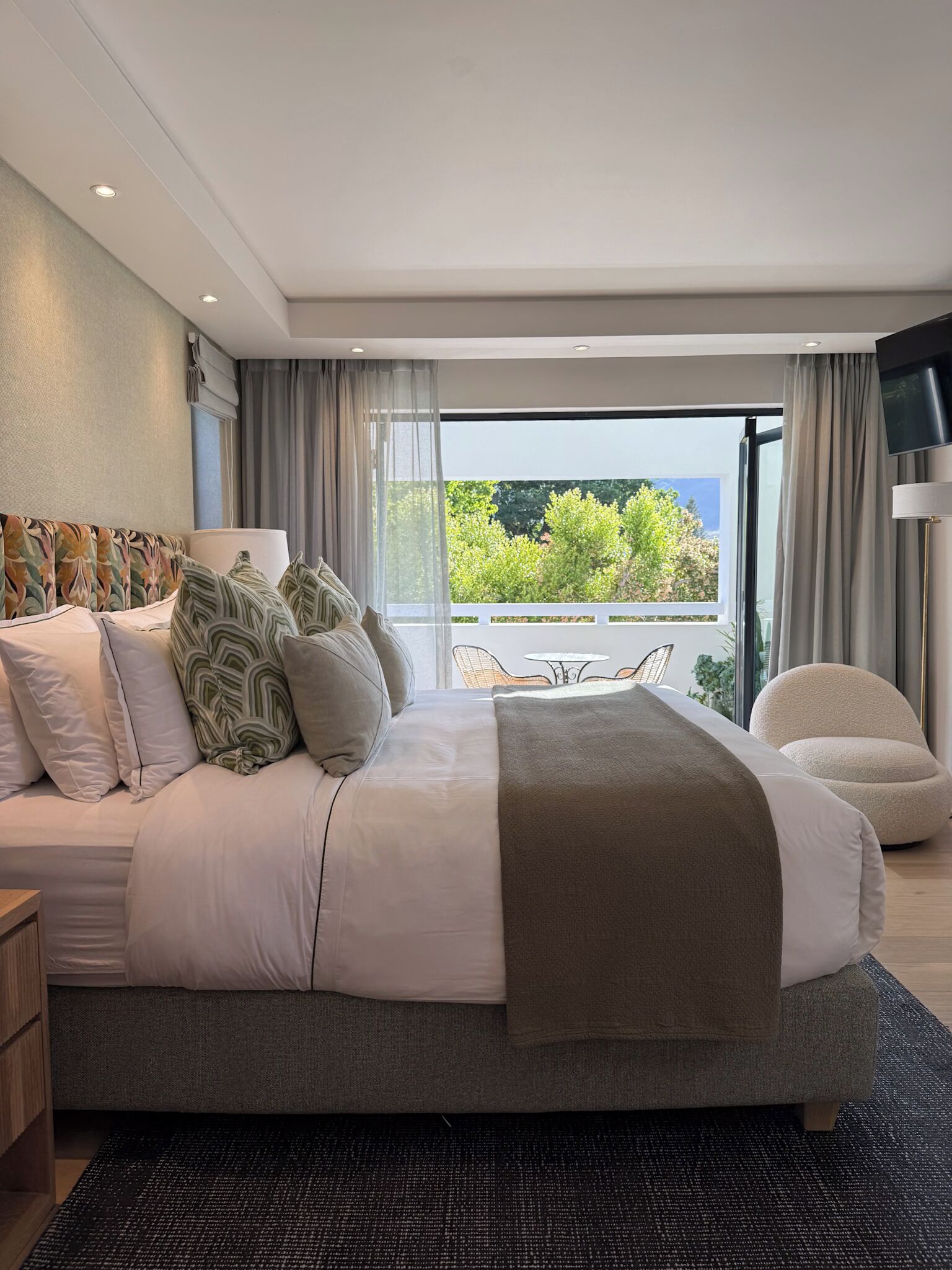Una camera da letto moderna con un letto grande, una TV e un balcone con vista sul verde.