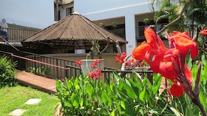 A thatched-roof structure, a wooden deck, and red flowers in a garden area. - Pensao Guest Lodge (Mbombela)