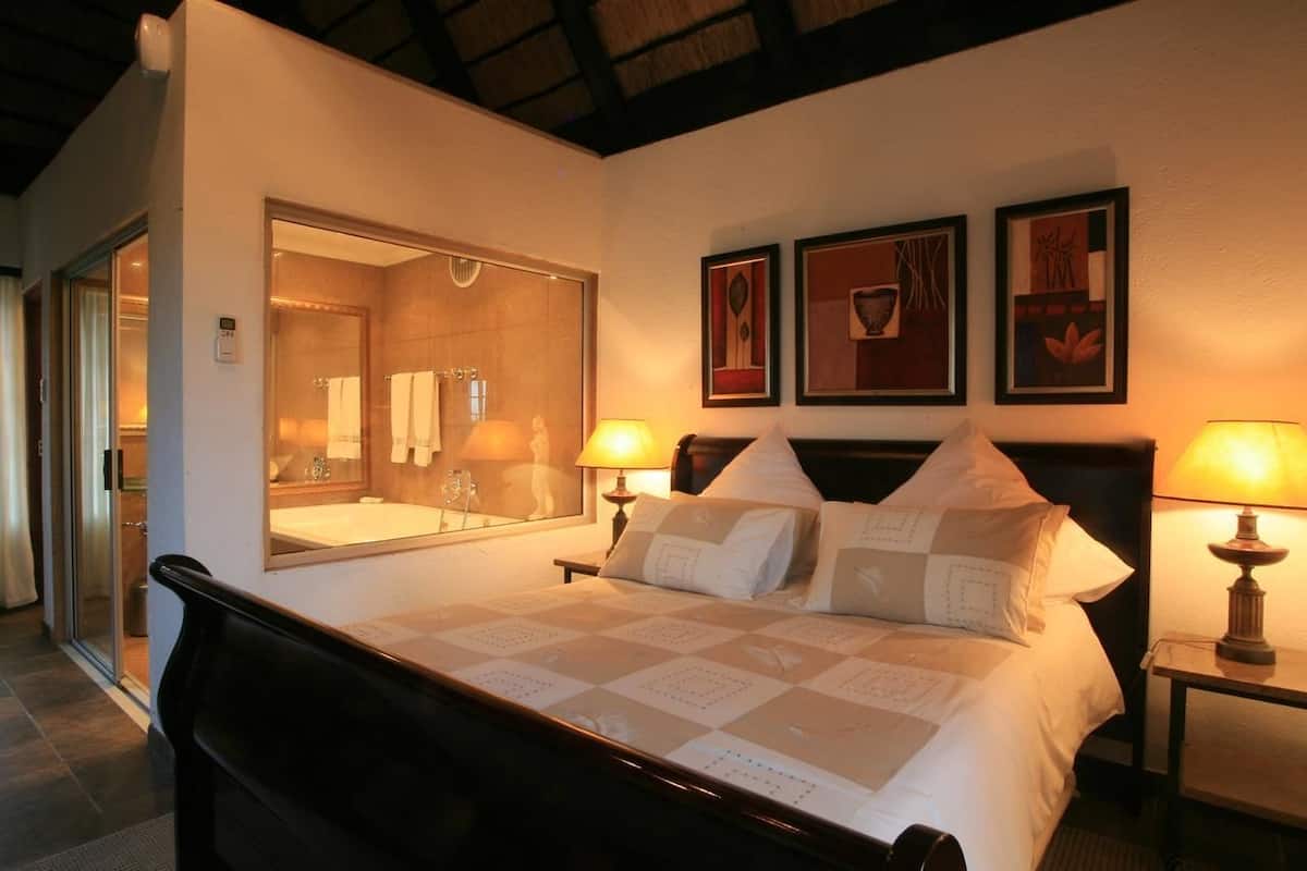 A hotel room with a large bed, two bedside lamps, a mirror, and three framed artworks on the wall.