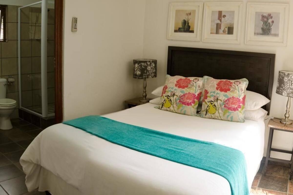 A bedroom with a bed, a nightstand, a lamp, and a shower area.