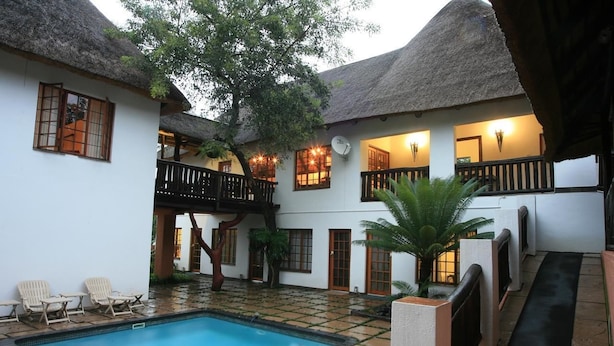 A courtyard with a swimming pool, white walls, thatched roofs, and outdoor seating. - Pensao Guest Lodge (Mbombela)
