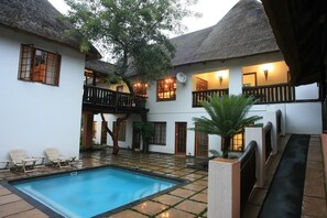 A courtyard with a swimming pool, white walls, thatched roofs, and outdoor seating. - Pensao Guest Lodge (Mbombela)