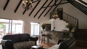 A spacious living area with a high ceiling, a staircase, and a kitchen area with a bar counter. - Pensao Guest Lodge (Mbombela)