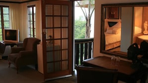 A room with a bed, a desk, a chair, a television, and a large window with a view of greenery. - Pensao Guest Lodge (Mbombela)