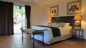 A neatly arranged hotel room with a bed, two bedside tables with lamps, a bench, and a view through a glass door. - Pensao Guest Lodge (Mbombela)