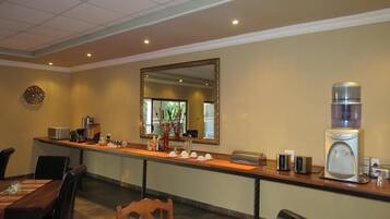 A hotel reception area with a long counter, a large mirror, and various amenities like a coffee machine, a water dispenser, and a small refrigerator.