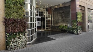 Une entrée moderne avec une porte en verre, une façade en briques et un petit espace jardin agrémenté de plantes.