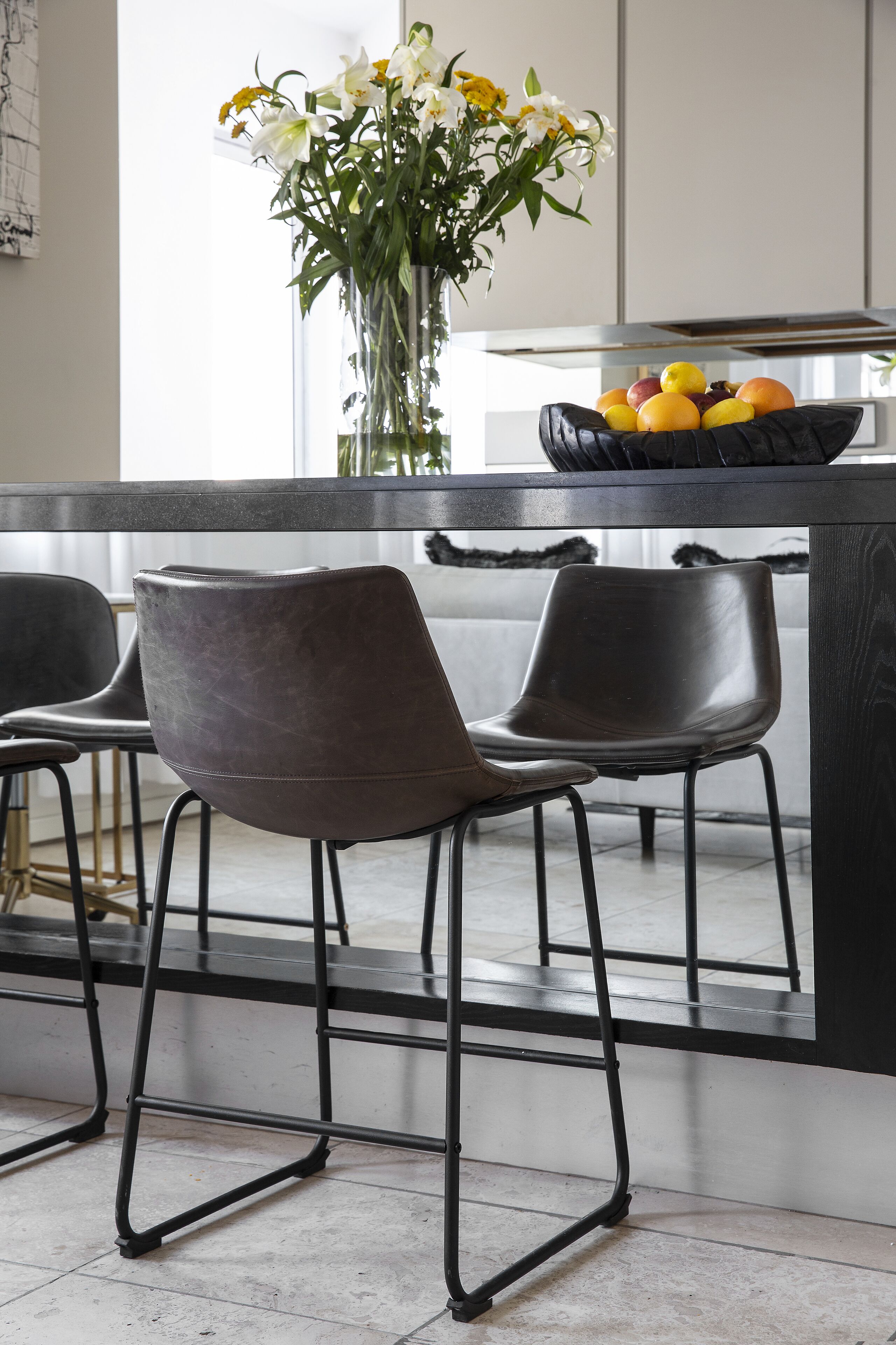 A modern kitchen with a black countertop, two bar stools, and a vase with flowers.
