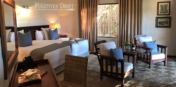 Quarto de hotel com cama, uma cadeira, uma mesinha e janela com cortinas.