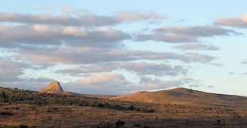 Paisagem com uma colina imponente e uma área plana com vegetação escassa.