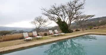 Piscina com espreguiçadeiras e vista para uma paisagem montanhosa.
