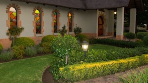 A building with a thatched roof, arched windows, and a well-maintained garden with hedges and yellow flowers.