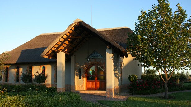 A building with a thatched roof, a central arched entrance, and a well-maintained garden.