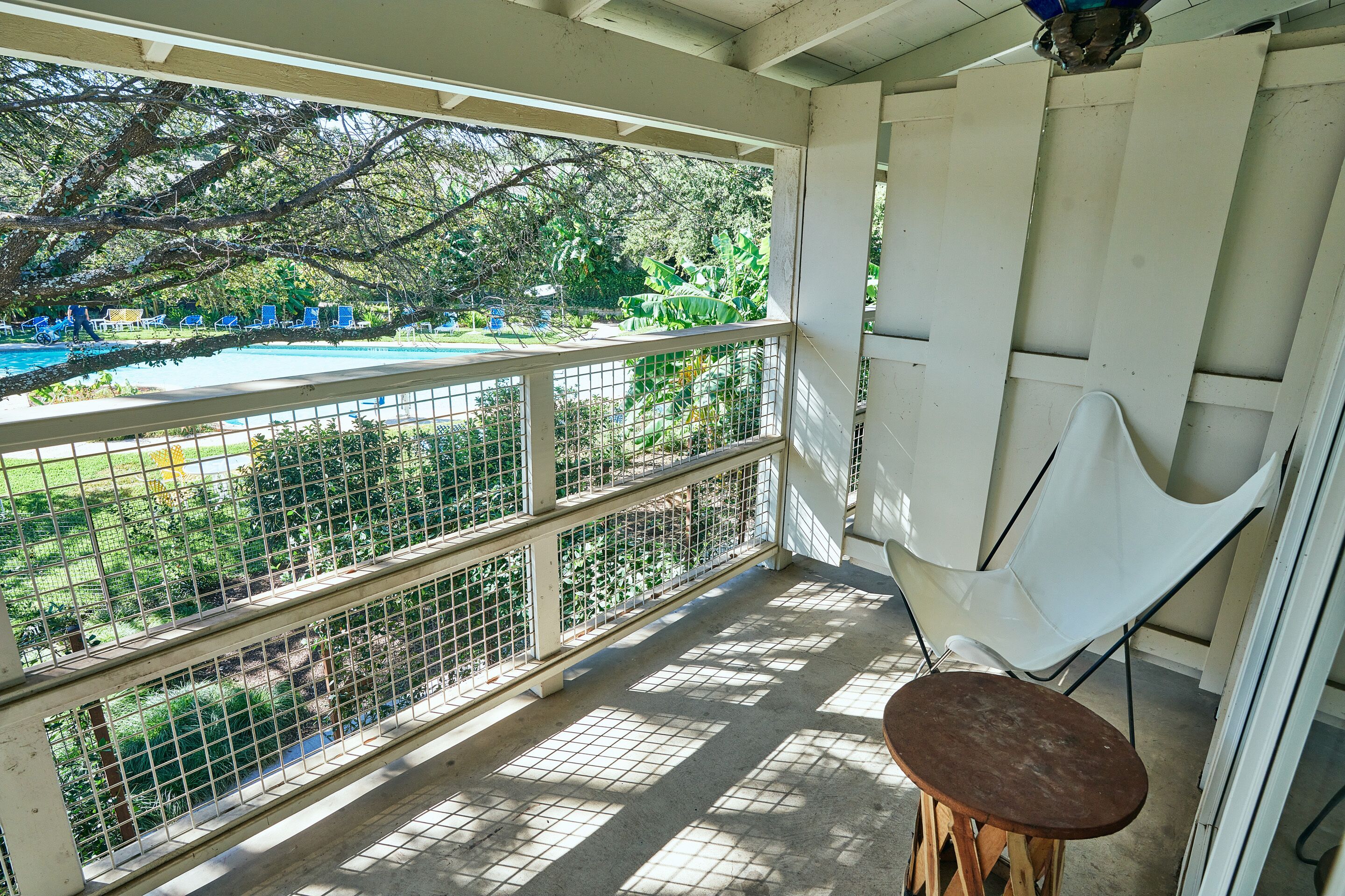Un balcon avec vue sur la piscine, une chaise blanche et un tabouret en bois.