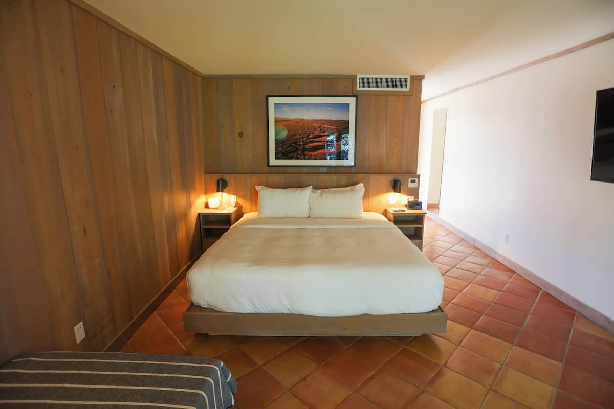 A bedroom with a large bed, wooden panel walls, a framed picture above the bed, and two bedside lamps.