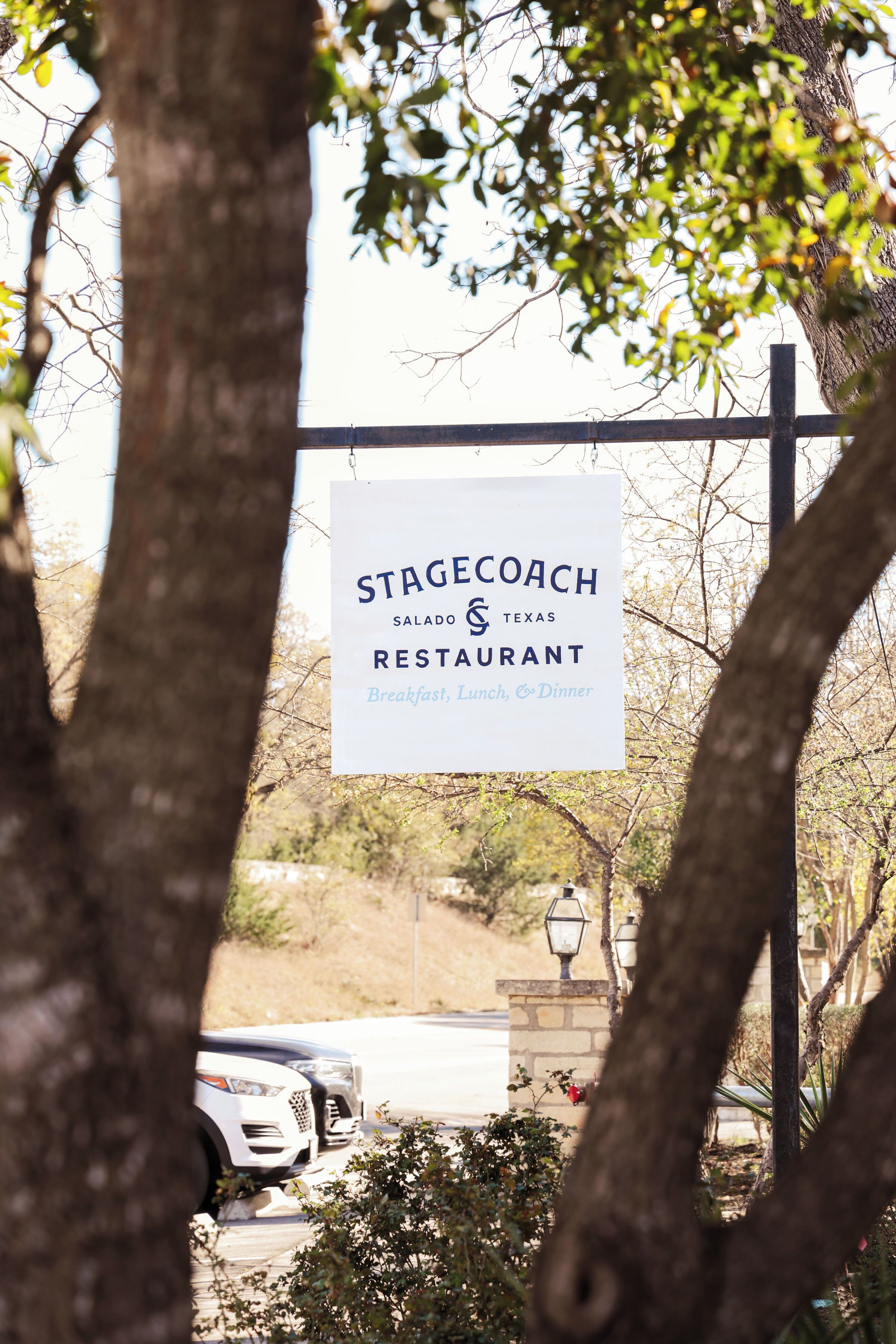 A sign for Stagecoach Restaurant with a view of parked cars and trees in the background.