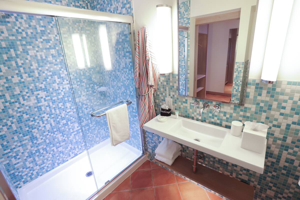 A bathroom with a glass shower enclosure, a white sink, and a mirror.