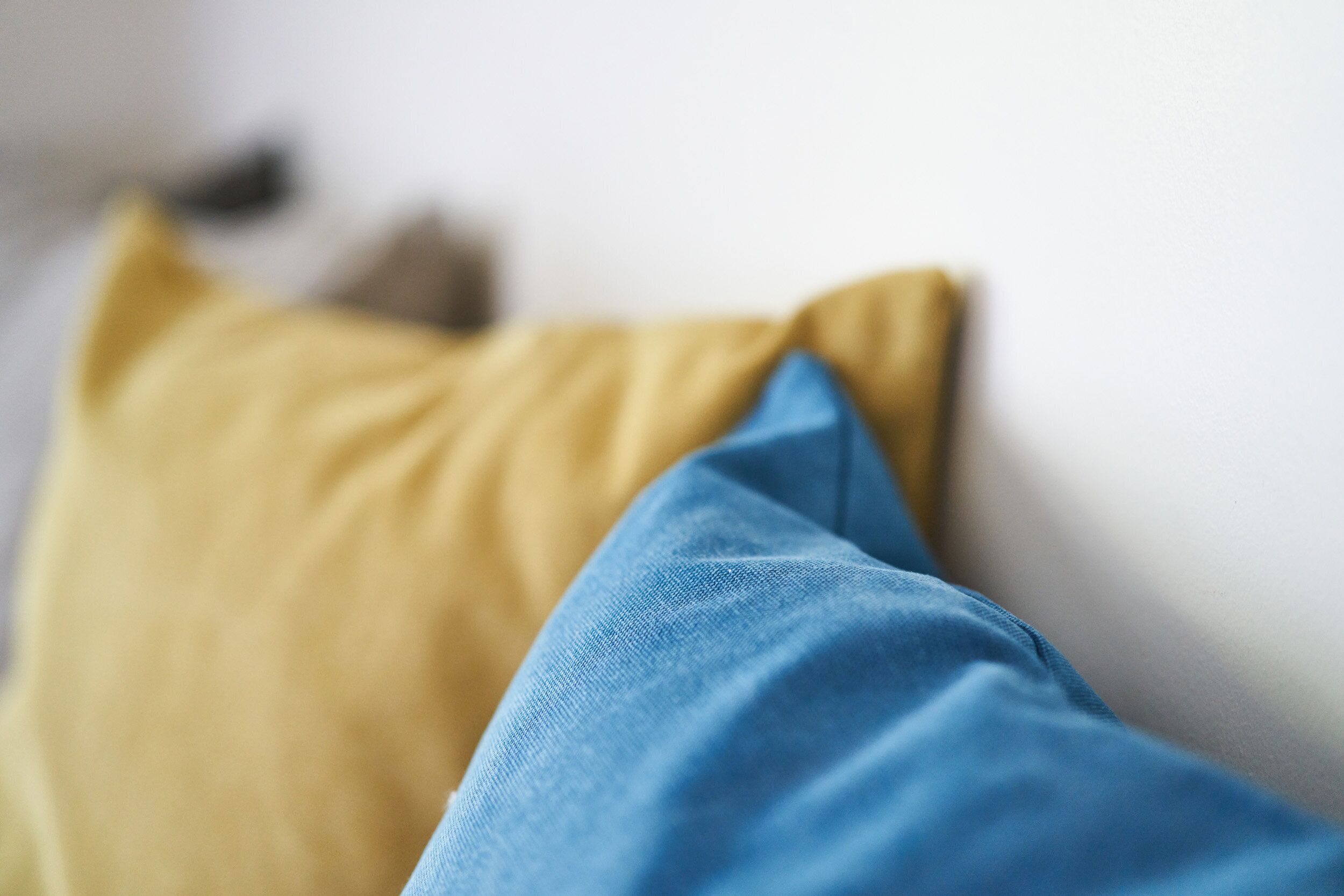 A close-up of two pillows, one yellow and one blue, on a white surface.