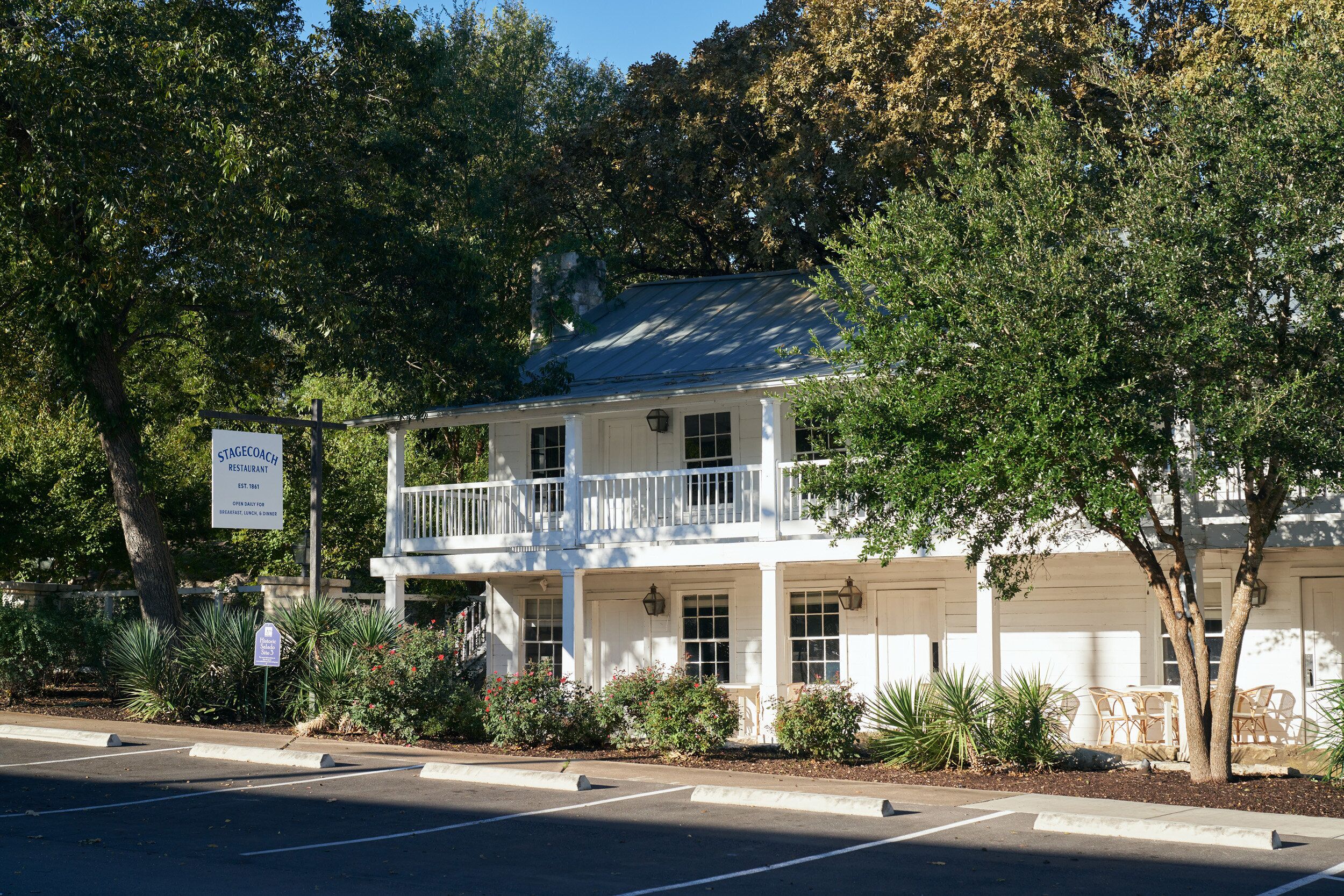 A two-story building with a balcony, surrounded by trees and shrubs.