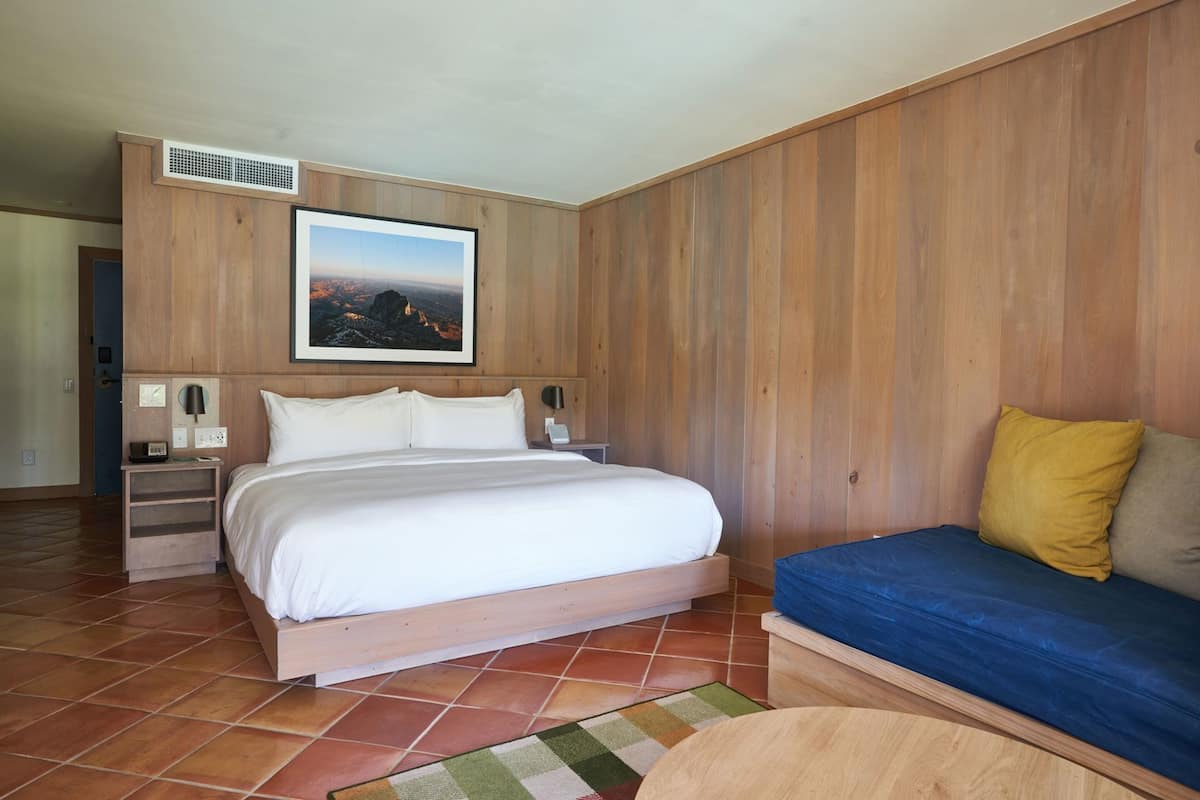 A bedroom with a bed, bedside tables, a wall-mounted picture, a sofa, and a patterned rug.