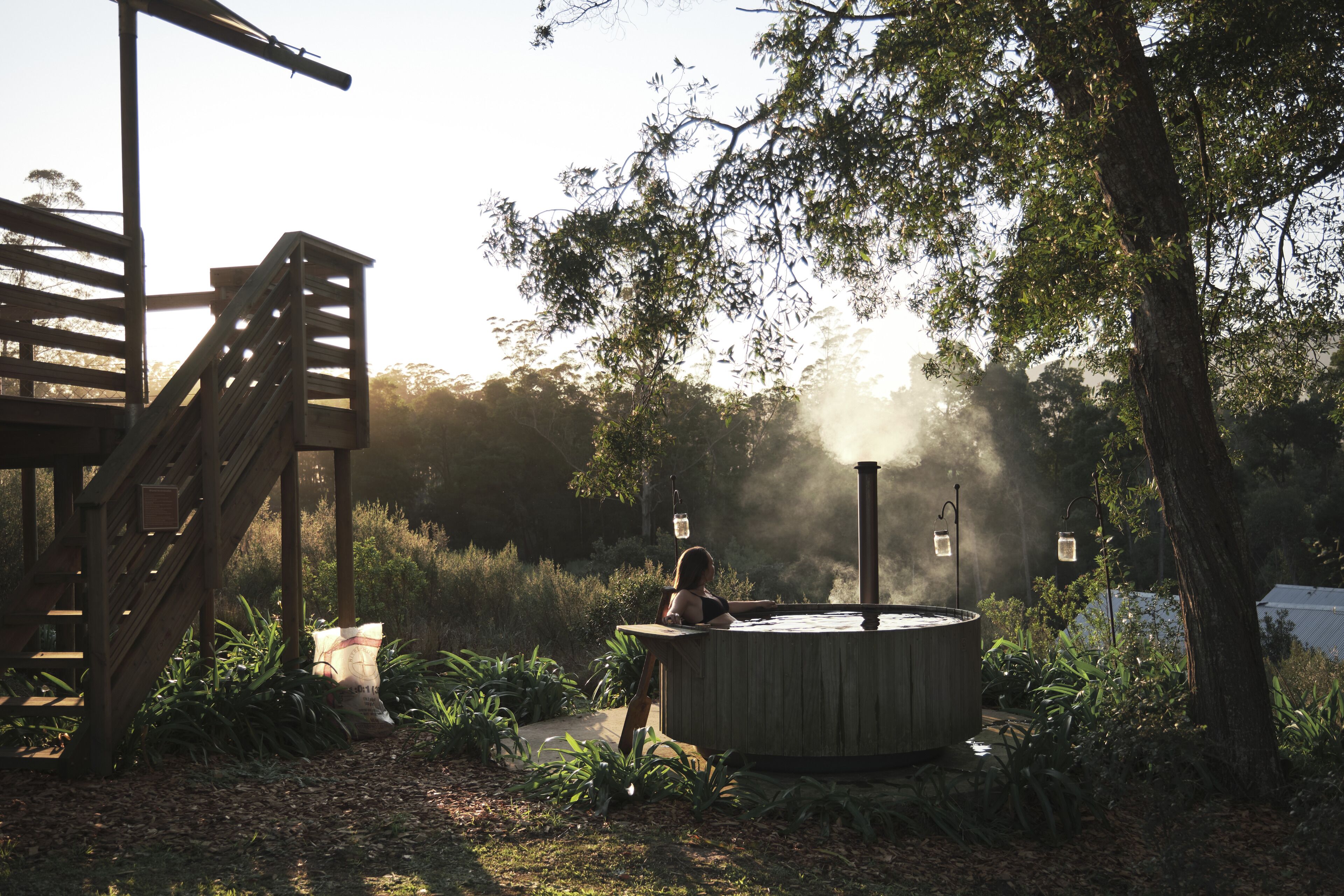 A hot tub in a garden with a wooden deck and a staircase.