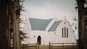 Une église blanche avec un toit vert, une entrée en arc de cercle et une clôture en bois à l’avant.