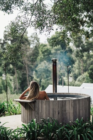 Une personne se détend dans un bain à remous en bois, entourée de verdure.