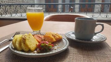 A breakfast setting with a plate of fruit, a glass of orange juice, and a cup on a table.
