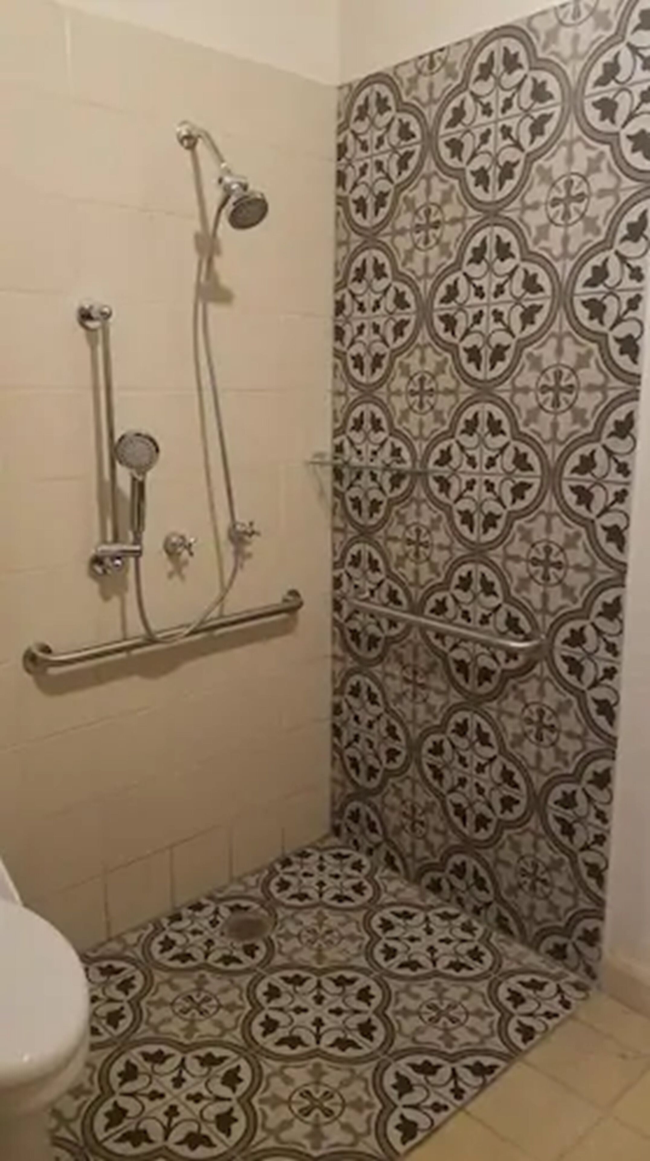 Chuveiro com parede de azulejos estampados e barra de apoio de metal.