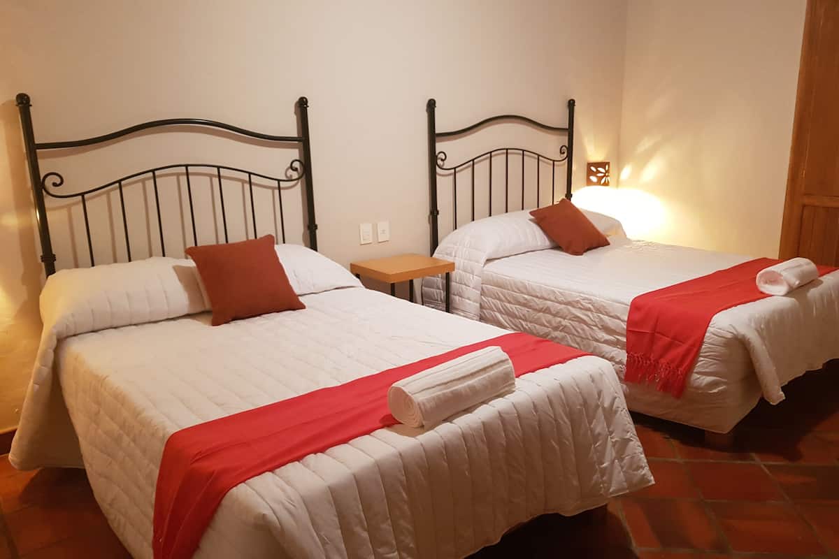 Deux lits simples avec des têtes de lit en métal, du linge de lit blanc et des touches de couleur rouge.