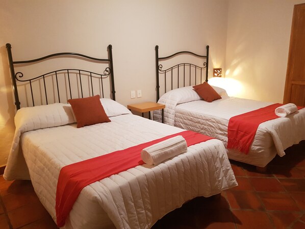 Dos camas individuales con cabeceros metálicos, ropa de cama blanca y detalles en rojo.