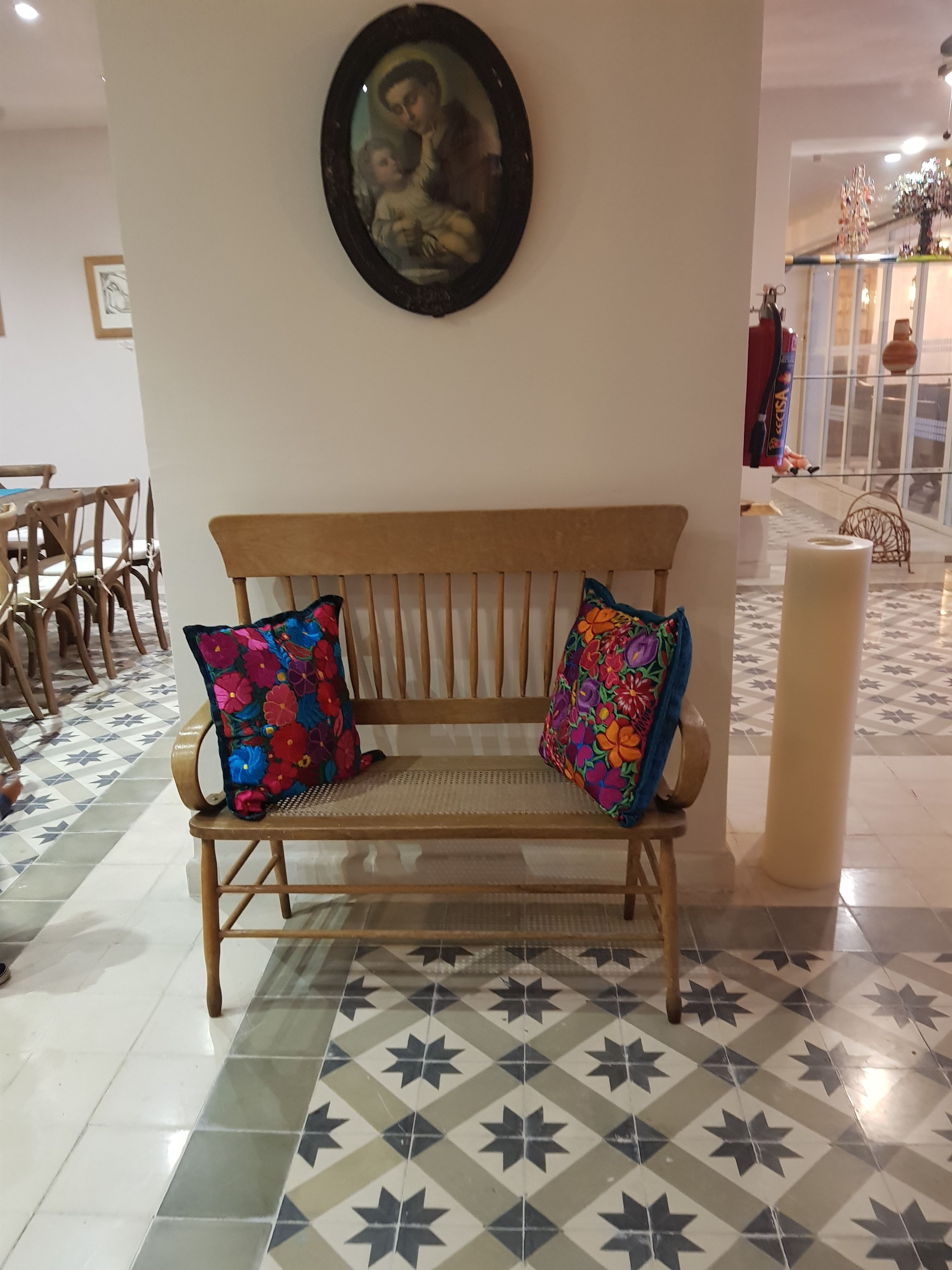 A wooden bench with colorful floral cushions, a framed picture above it, and a patterned floor.