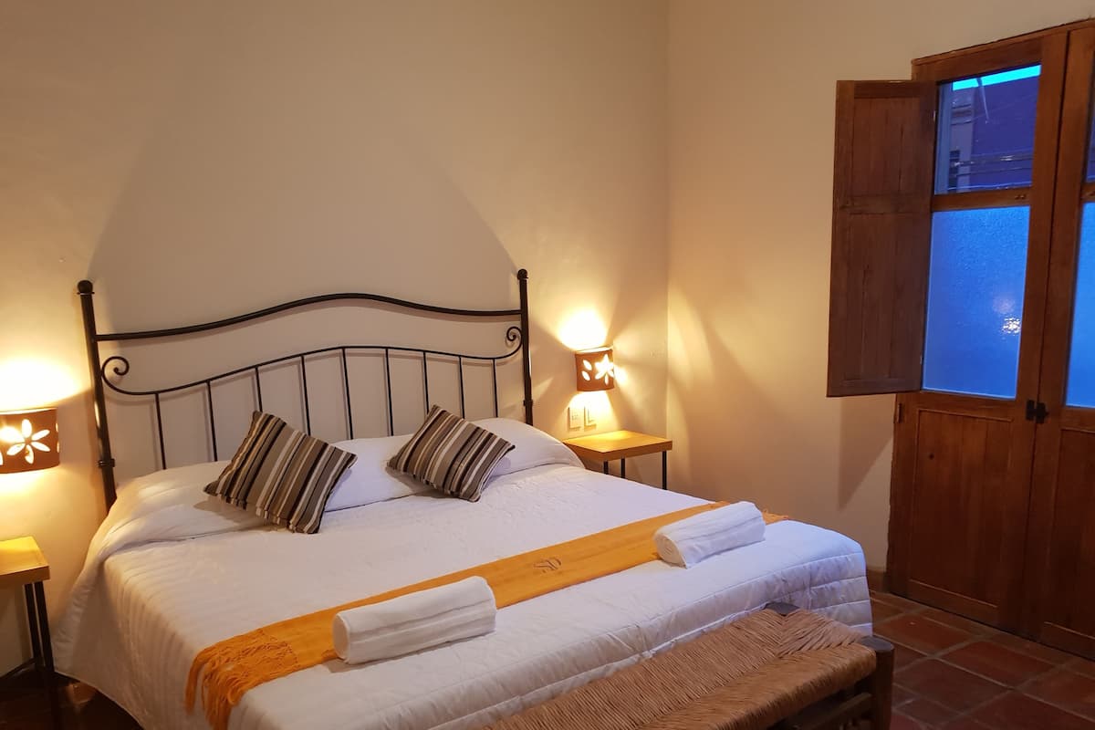 Un lit bien fait, agrémenté d’oreillers à rayures, un banc en bois et deux lampes de chevet.