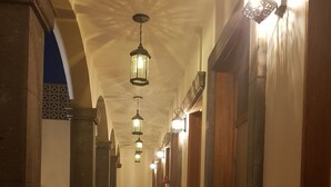 Un couloir doté d’un sol carrelé, de luminaires fixés aux murs et de portes en bois.
