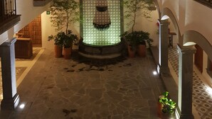 Une cour intérieure avec une fontaine centrale, des plantes en pot et un mur orné de motifs.
