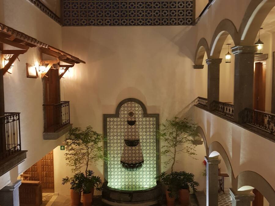 A courtyard with a central fountain, potted plants, and a patterned wall.