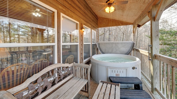 Une terrasse en bois avec un jacuzzi, des bancs en bois et un ventilateur de plafond.