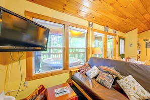 Un salon confortable avec un téléviseur à écran plat, un plafond en bois et de grandes fenêtres donnant sur un jacuzzi.
