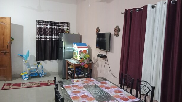 Un espace de vie compact comprenant une table à manger, un réfrigérateur, un téléviseur fixé au mur et une fenêtre avec des rideaux.