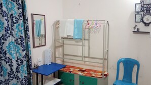 Une chambre avec un lit superposé, une chaise bleue, une petite table, un miroir et une horloge murale.